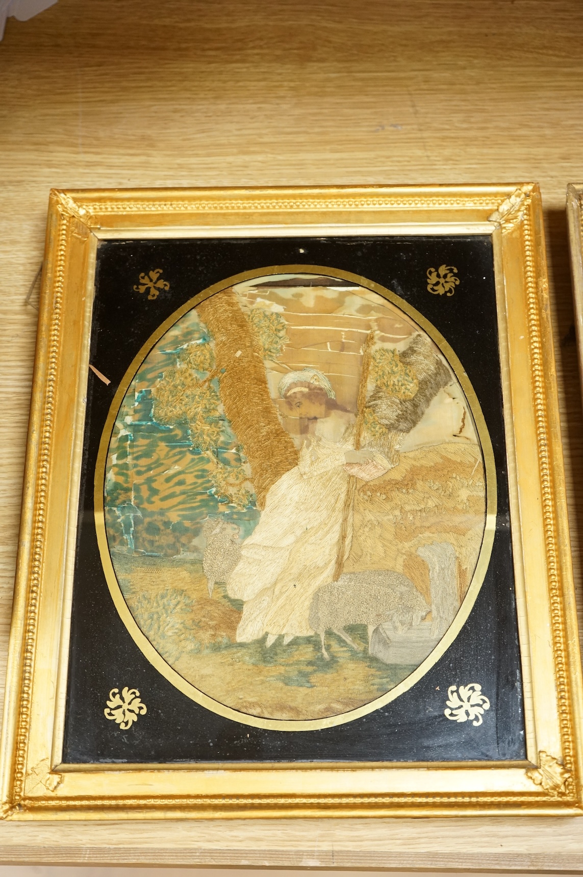 A pair of oval framed early 19th century silk embroideries of a Shepherd and Shepherdess mounted in Verre eglomise glass and gilt frames. Embroideries 28cm high